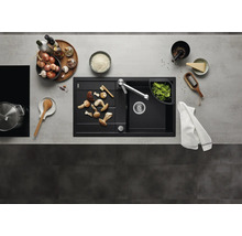 Évier encastrable moderne noir avec égouttoir et robinet de cuisine dans une cuisine organisée avec des ustensiles et des aliments frais.