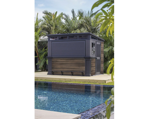 Modernes Gartenhaus mit Bartheke auf Holzterrasse neben einem Swimmingpool, umgeben von tropischen Pflanzen.