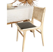 Chaise de salle à manger en bois clair avec dossier en cannage et coussin foncé à côté d une table avec nappe blanche