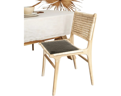 Chaise de salle à manger en bois clair avec dossier en cannage et coussin foncé à côté d une table avec nappe blanche