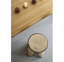 Tabouret rond avec assise moelleuse et tressage en rotin, placé à côté d'une table en bois massif avec boules décoratives et une bougie.