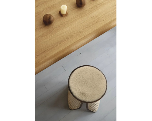 Tabouret rond avec assise moelleuse et tressage en rotin, placé à côté d'une table en bois massif avec boules décoratives et une bougie.