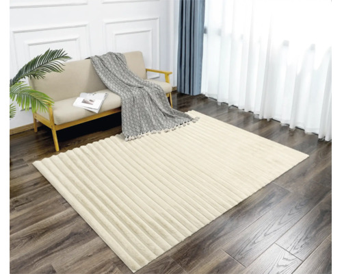 Ein rechteckiger Teppich mit strukturierter Streifenoptik liegt in einem hellen Wohnzimmer vor einem Sofa mit Decke.