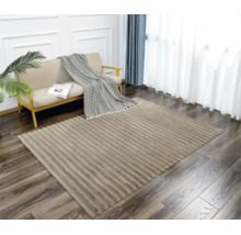 Ein moderner Wohnzimmerteppich mit gerippter Struktur auf einem Holzboden vor einem Sofa mit Überwurf und Zimmerpflanze in einem hellen Raum.