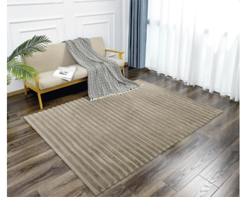 Ein moderner Wohnzimmerteppich mit gerippter Struktur auf einem Holzboden vor einem Sofa mit Überwurf und Zimmerpflanze in einem hellen Raum.