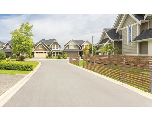 Eine ruhige Wohnstrasse mit Einfamilienhäusern und einem modernen Sichtschutzzaun aus Holz im Vorgartenbereich.