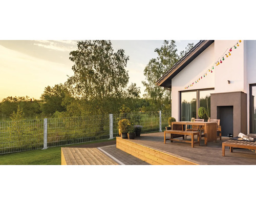 Moderne Holzterrasse mit Sitzgruppe aus Holz und einem Doppelstabmattenzaun im Garten bei Sonnenuntergang.