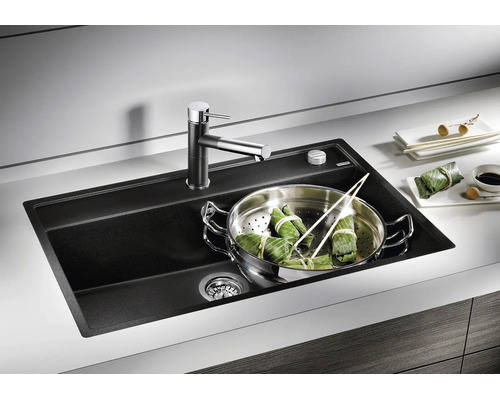 Moderne schwarze Einbauspüle aus Verbundwerkstoff mit Armatur in einer hellen Küchenarbeitsplatte und einem Dämpfeinsatz im Becken.