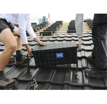 Zwei Handwerker tragen eine schwarze Aluminium Werkzeugkiste von Alutec auf einem mit Dachziegeln gedeckten Hausdach.