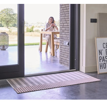 Un tapis couloir rayé devant une grande porte-fenêtre donnant sur une femme assise à une table de jardin.