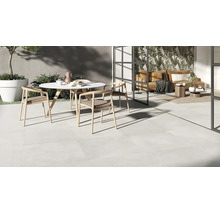 Terrasse moderne avec carrelage clair, table ronde et transition vers un espace de vie lumineux avec vitrage toute hauteur.