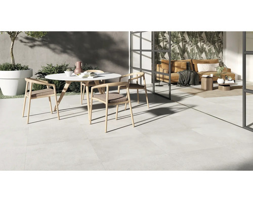 Terrasse moderne avec carrelage clair, table ronde et transition vers un espace de vie lumineux avec vitrage toute hauteur.