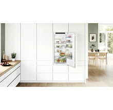 Einbaukühlschrank in moderner, weisser Einbauküche mit offener Tür, gefüllt mit frischen Lebensmitteln und Bosch Logo.
