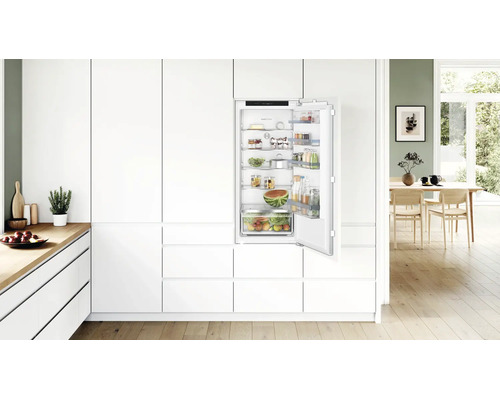 Einbaukühlschrank in moderner, weisser Einbauküche mit offener Tür, gefüllt mit frischen Lebensmitteln und Bosch Logo.