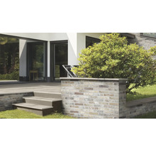 Moderne Terrasse mit einer Mauer aus Klinkerriemchen und einer Treppe aus Steinplatten vor einem hellen Wohnhaus mit grossen Fensterfronten.