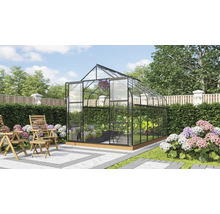 Serre autonome avec parois en verre et cadre en métal dans un jardin soigné avec des chaises en bois sur une terrasse.