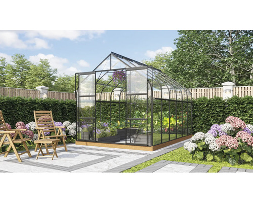 Serre autonome avec parois en verre et cadre en métal dans un jardin soigné avec des chaises en bois sur une terrasse.