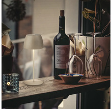 Une petite lampe LED sans fil rechargeable sur un rebord de fenêtre à côté d une bouteille de vin, de verres et d une plante, éclairage d ambiance.
