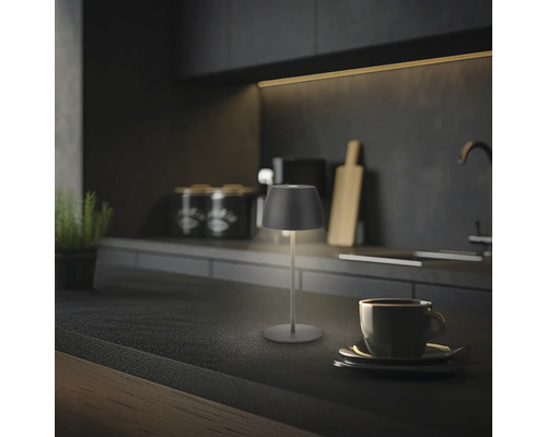 Moderne LED Tischleuchte auf einer Küchenarbeitsplatte neben einer Kaffeetasse in einer stilvollen dunklen Küche.