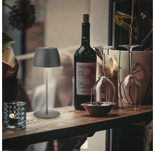 Moderne LED Tischleuchte fuer den Innen und Aussenbereich platziert auf einer rustikalen Holztheke neben einer Flasche Wein und Weinglaesern.