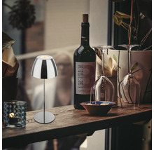 Lampe de table LED moderne en métal sur une bouteille, posée sur une table en bois avec bouteille de vin et verres.