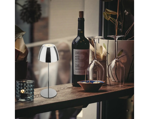 Lampe de table LED moderne en métal sur une bouteille, posée sur une table en bois avec bouteille de vin et verres.
