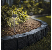 Zwei moderne LED Solarleuchten als Erdspießleuchten für die Gartenbeleuchtung in einem Blumenbeet entlang einer Steinmauer.