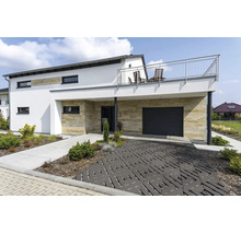 Modernes Einfamilienhaus mit Natursteinverkleidung, Garage, Balkon mit Edelstahlgeländer und dekorativ gepflasterter Einfahrt im Vorgarten.
