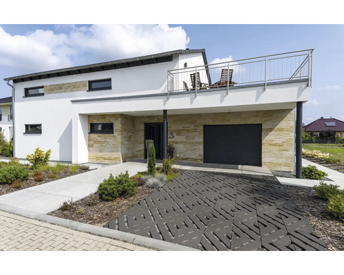 Modernes Einfamilienhaus mit Natursteinverkleidung, Garage, Balkon mit Edelstahlgeländer und dekorativ gepflasterter Einfahrt im Vorgarten.