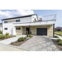 Modernes Einfamilienhaus mit Natursteinverkleidung, Garage, Balkon und einer Pflasterung aus Rasengittersteinen im Vorgarten.