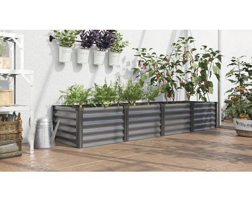 Jardinière surélevée rectangulaire en métal dans une serre avec diverses plantes comme des poivrons et des carottes sur un sol de terrasse.