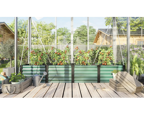 Großes Hochbeet aus Metall in einem Gewächshaus mit Tomatenpflanzen auf einer Holzterrasse mit Gießkanne und Holzkisten.