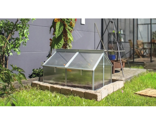 Ein Frühbeet mit Aluminiumrahmen und Hohlkammerplatten in einem Garten auf einer gemauerten Umrandung vor einer Hauswand.
