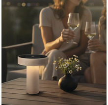 Moderne Solar Tischleuchte mit integriertem Solarpanel auf einem Terrassentisch neben einer Blumenvase bei zwei Personen mit Weingläsern.