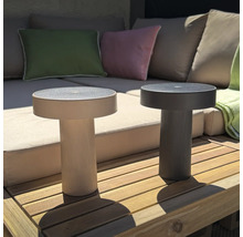 Zwei runde, moderne LED Tischleuchten mit geriffeltem Standfuß auf einer Holzterrasse vor einem Lounge Sofa.