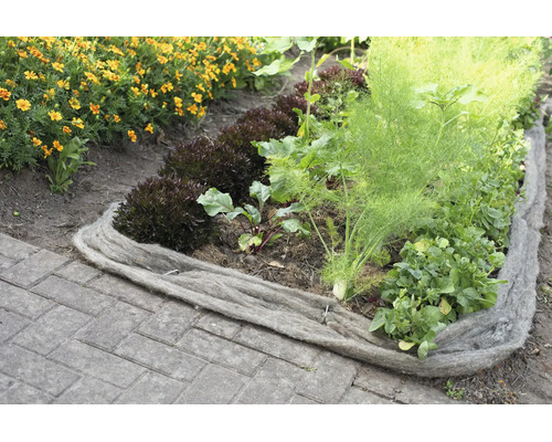 Bordure de jardin en laine de mouton servant de barrière naturelle pour un potager avec des légumes et des fleurs sur un sol pavé.