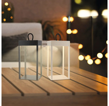 Zwei moderne LED Tischleuchten in Laternenform mit Tragegriff stehen auf einem Holztisch auf einer Terrasse in abendlicher Atmosphäre.
