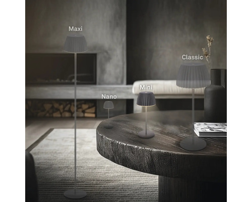 Vier LED Lampen mit plissiertem Schirm in den Größen Maxi, Nano, Mini und Classic in einem modern eingerichteten Wohnzimmer mit Kamin.