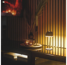 Eine kleine Tischlampe leuchtet neben Teelichtern auf einem Tablett vor einer Wand mit Holzlamellen.