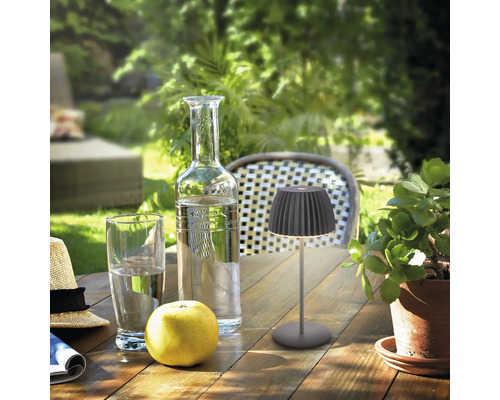 Moderne LED Tischleuchte für den Außenbereich auf einem Holztisch mit Glas Flasche Apfel und Pflanze im Garten bei Tageslicht