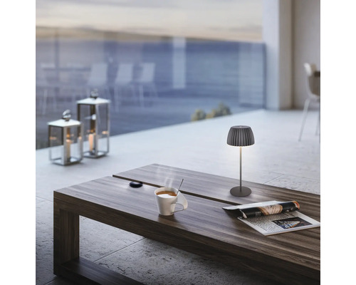Moderne kabellose LED Tischleuchte auf einem Holztisch mit Kaffeetasse und Zeitschrift auf einer Terrasse.