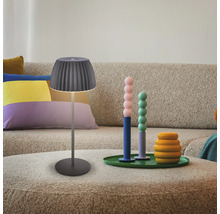 Moderne Tischleuchte mit plissiertem Lampenschirm auf einem Couchtisch vor einem Sofa mit dekorativen Accessoires in einem Wohnzimmer