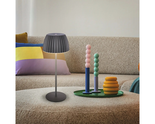 Moderne Tischleuchte mit plissiertem Lampenschirm auf einem Couchtisch vor einem Sofa mit dekorativen Accessoires in einem Wohnzimmer