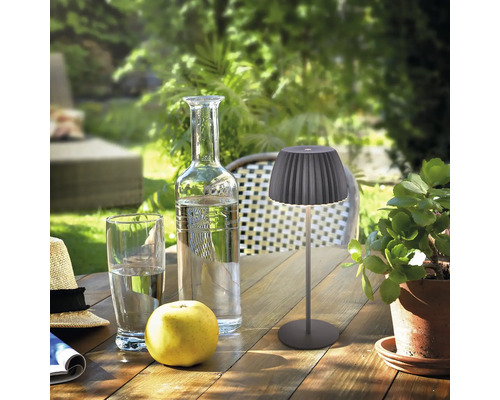 Moderne LED Akkuleuchte mit geriffeltem Lampenschirm auf einem Holztisch im Garten