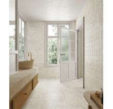 Salle de bains lumineuse avec carrelage imitation pierre naturelle au mur et au sol, meuble vasque avec vasque à poser, robinet doré et porte ouverte.