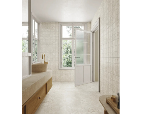 Salle de bains lumineuse avec carrelage imitation pierre naturelle au mur et au sol, meuble vasque avec vasque à poser, robinet doré et porte ouverte.