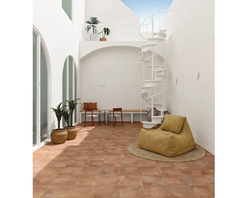 Cour intérieure lumineuse avec carrelage en terre cuite, escalier en colimaçon blanc, banc et pouf dans un design minimaliste et moderne.