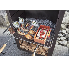 Grille de cuisson en métal avec poignées en bois au-dessus d une cheminée de jardin, garnie d aliments tels que saucisses, viande et légumes.
