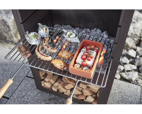 Grille de cuisson en métal avec poignées en bois au-dessus d une cheminée de jardin, garnie d aliments tels que saucisses, viande et légumes.