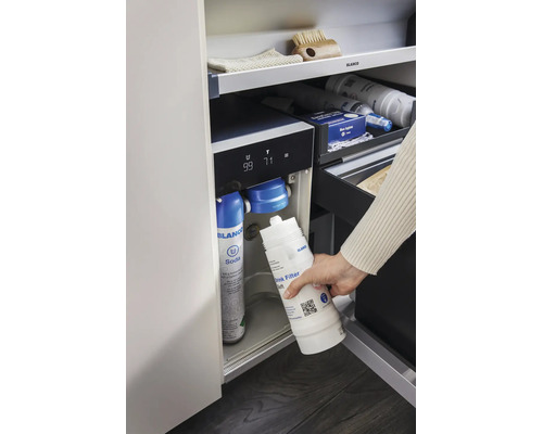 Une main remplace le filtre à eau dans un système d eau Blanco avec bouteille de gaz carbonique dans une armoire de cuisine.
